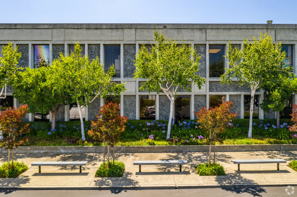 Aerial of landscaping of 7901 Oakport. Delicate green trees and blooming purple flowers line windowed walls. exterior