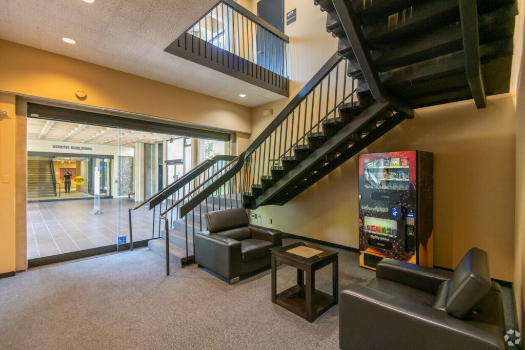 Common stairwell and small seating area of 7901 Oakport. Entryway is seen through floor-to-ceiling windows.