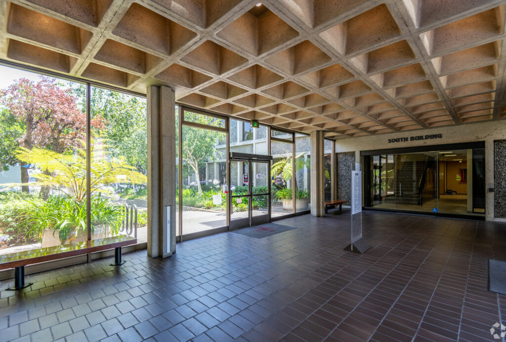 View from the Lobby of the South Building. Floor to ceiling windows show trees and flowers in the courtyard.