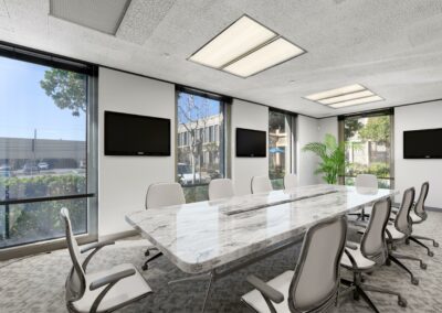 Large conference room in suite. Long marble desk, surrounded by 10 chairs and mounted TVs. 4 wall-height windows.