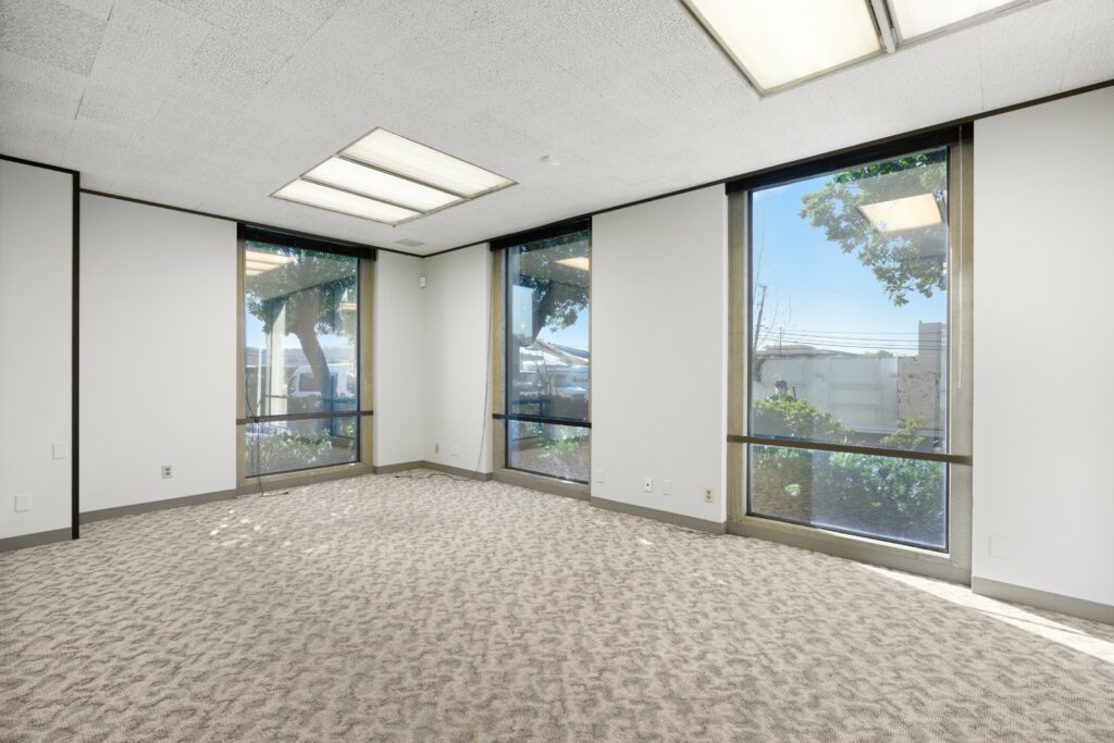 Conference room in Suite. Three floor-to-ceiling windows face trees and other office buildings.