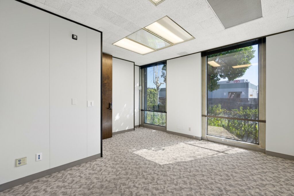 Large private office in Suite. Two floor-to-ceiling windows face trees and other office buildings.