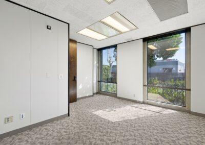 Large private office in Suite. Two floor-to-ceiling windows face trees and other office buildings.