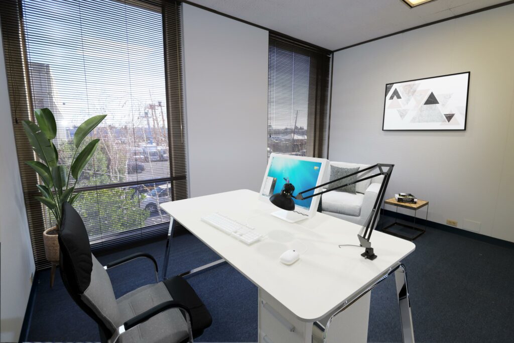 Virtually staged private office with desk and small seating area in Suite. Two floor-to-ceiling windows.