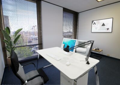 Virtually staged private office with desk and small seating area in Suite. Two floor-to-ceiling windows.